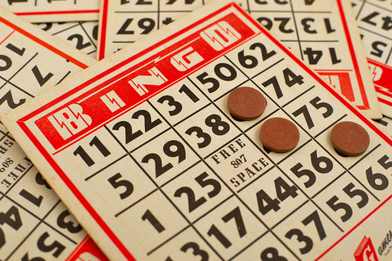 A pile of red and white Bingo cards. The top card shows a full card with two markers on it.