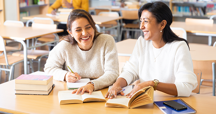 Literacy Volunteers header showing smiling woman teaching another woman with open books in front of them on a desk