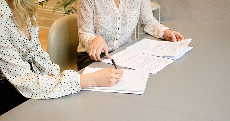 Women in business attired looking over legal documents at meeting table