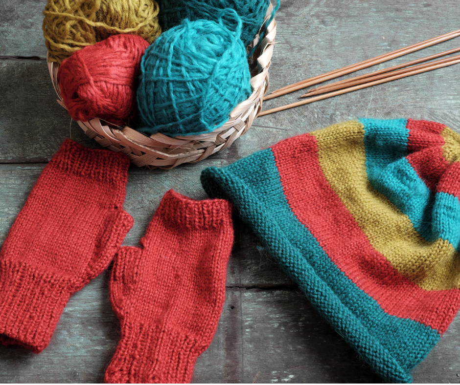 basket of yarn with knitting needles, mittens, and a hat