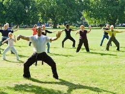 a group of people practice tai-chi with out stretched arms on a field
